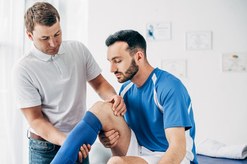 Physiotherapist massaging leg of handsome football player in hospital