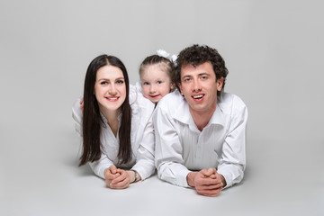 Portrait of a happy family. Parents are leaning on elbows and their daughter hugging them. On white background.