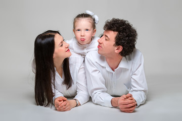 Portrait of a happy family. Parents are leaning on elbows and their daughter hugging them. Girl shows language. On white background.