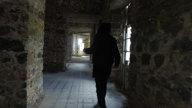 WIDE DOLLY IN: Young man disguised in black clothing explores inside old derelict stone building