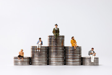 Miniature people sitting on piles of coins.