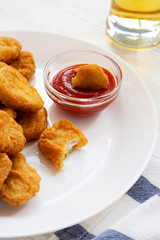 Chicken nuggets with ketchup and glass of cold beer on a white wooden background, low angle view. Close-up.
