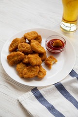 Chicken nuggets with ketchup and glass of cold beer on a white wooden table, low angle view.