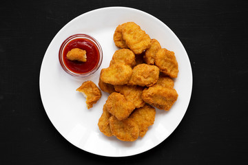 Chicken nuggets with ketchup on a white plate on a black background, overhead view. Flat lay, from above, top view. Close-up.