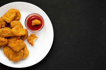 Chicken nuggets with ketchup on a white plate on a black background, top view. Flat lay, overhead, from above. Copy space.