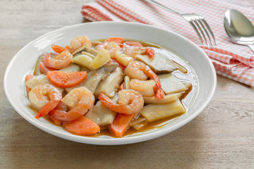 close up of stir fried king oyster mushroom with shrimp in a ceramic dish on wooden table. asian homemade style food concept.