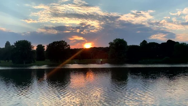 Sunset at dusk at the lake. Sunbeams are reflected in the water. Aasee Muenster, Germany 4K