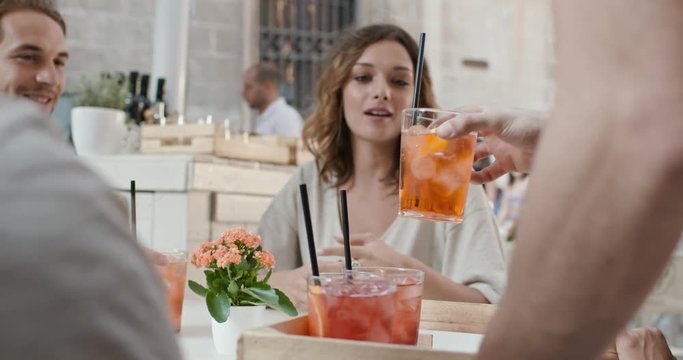 Waiter brings cocktails to four people or two couples at aperitif in city cafe.Medium portrait shot Friends italian trip in Umbria.4k slow motion