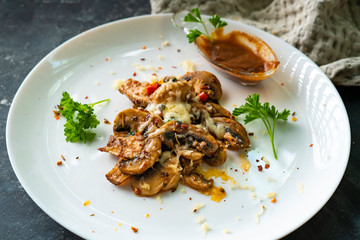 roasted champignons with cheese sauce in a white ceramic plate with herbss