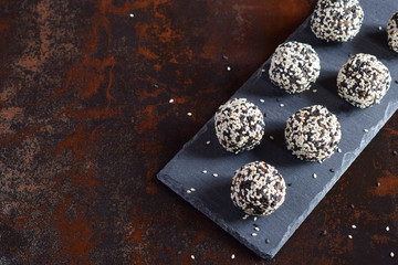 Healthy raw energy bites with flax seeds, almonds, banana and dates. Vegan truffles in sesame seeds on dark background. Homemade candy balls. Raw food. Gluten free. Dairy free.