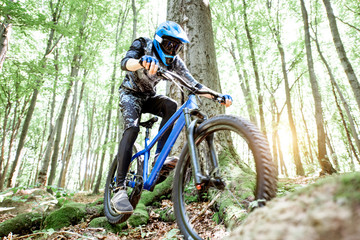 Fototapeta premium Professional well equipped cyclist riding downhill on the off road in the forest. Concept of an extreme sport and enduro cycling