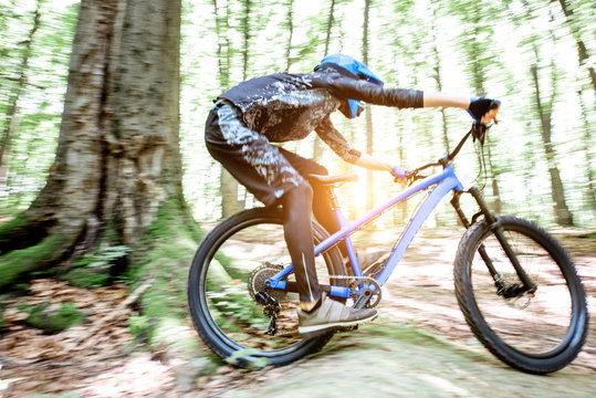 Professional well equipped cyclist riding downhill on the off road in the forest. Concept of an extreme sport and enduro cycling. Image with motion blur