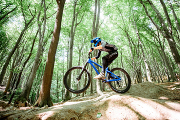 Professional well equipped cyclist riding on the forest track with slides for jumping. Concept of an extreme sport and enduro cycling. Image with motion blur