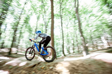 Professional well equipped cyclist riding on the forest track with slides for jumping. Concept of...