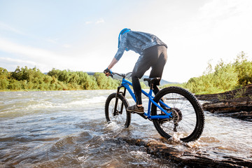 Professional well-equipped cyclist riding on the rocky riverside in the mountains. Concept of a freeride cycling and extreme sport