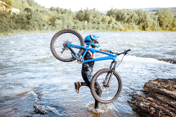 Professional well-equipped cyclist jumping with bicycle on the riverside in the mountains. Concept of a freeride and off road cycling