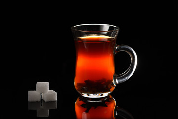 A glass of Turkish black tea on the black background with sugar