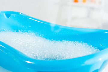 selective focus of blue baby bathtub with water and bath foam