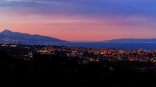 Timelapse day to night view of a sunset on the town of Acireale in Sicily, with the southern tip of Italy on the background