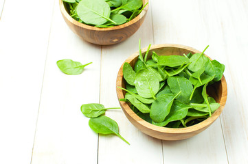 Fresh green spinach leaves on wooden bowl on white wooden rustic background top view copy space. Baby young spinach leaves, Ingredient for salad, healthy food, diet. Nutrition concept.