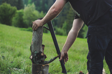 The guy is cutting an old tree in the mountains with an ax. Ukrainian Carpathian Mountains. Bonfire. Tourism. Ax