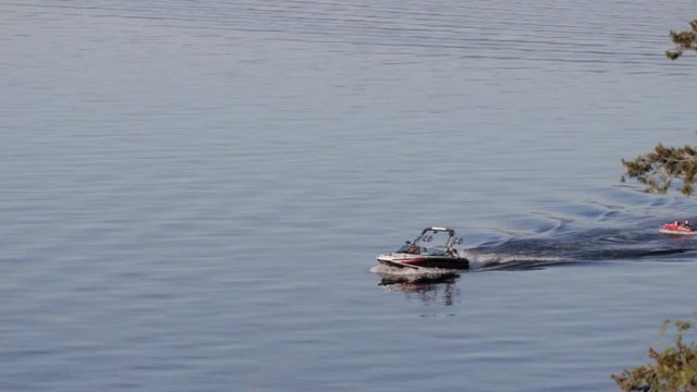 Motorboat Pulling Kids In Tube Across Lake In Summer