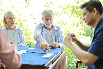 Caucasian husband dealt cards on gaming table with elder multiethnic family with serious face