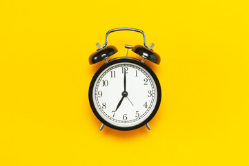 Black retro alarm clock on yellow background top view Flat lay copy space. Minimalistic background,...