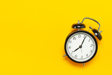 Black retro alarm clock on yellow background top view Flat lay copy space. Minimalistic background,...