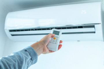 Air conditioner temperature adjustment with remote controller in room at home.