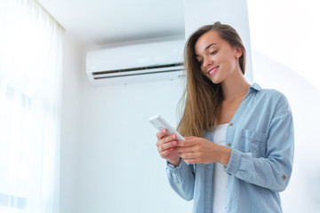 Young attractive woman control air conditioner temperature using remote controller in room at home.