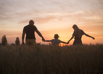 Fototapeta na wymiar man with children stand hand in hand in the field in the evening