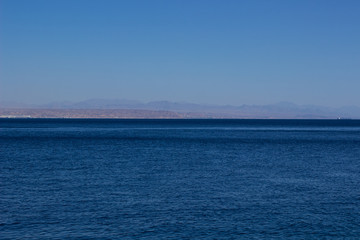 Obraz premium idyllic sea smooth water surface with view opposite waterfront and mountain silhouette background nature scenery wallpaper landscape with empty copy space 