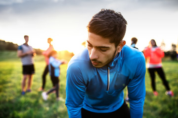 Fototapeta premium A portrait of young man with large group of people doing exercise in nature.