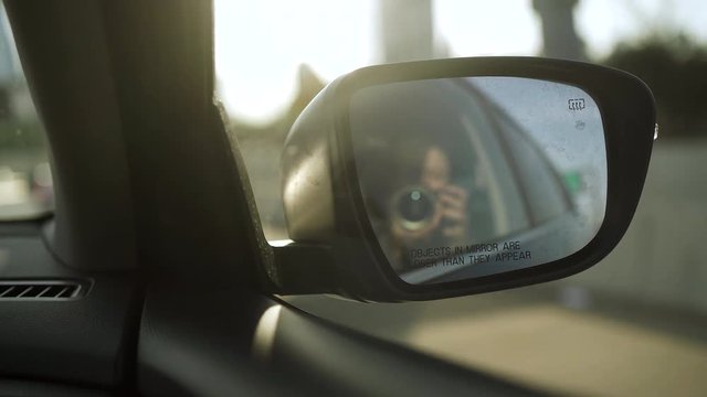 Happy woman doing selfie with professional camera in a car mirror and smiling in moving car.
