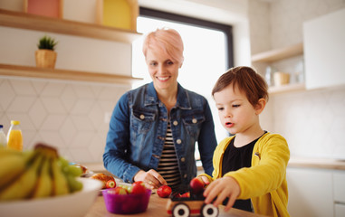 A young mother with small daughter eating fruit in a kitchen.