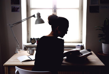 A rear view of young female student sitting at the table, studying.