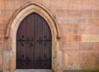 Fototapeta na wymiar Church entrance door with wrought iron recessed into a colourful textured sandstone pointed archway