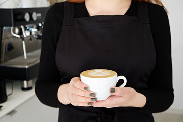 Portrait of young beautiful barista woman wearing blank stylish black apron making cappucino hot beverage in hipster coffee place. Close up, copy space, background.