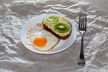 Delicious and healthy breakfast. Fried eggs and kiwi sandwich on a white plate, close-up, space for text