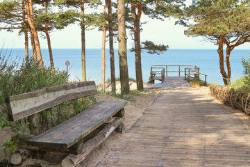 Fototapeta na wymiar Resting area at sandy beach of the Baltic Sea. Wooden footpath leading to sea with wooden bench and terrace.