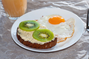 Healthy and tasty breakfast, juice, wholegrain sandwich with kiwi and fried egg on white plate