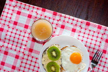 Healthy and tasty breakfast, quince juice, whole-grain bread sandwich with kiwi and egg on white plate, pink napkin