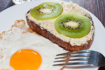 Healthy, tasty breakfast, juice, whole-grain bread sandwich, kiwi and fried egg on a white plate, on wooden table