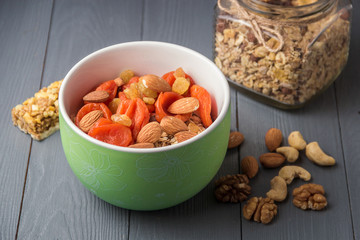 Granola cereal flakes with dried fruit, nuts in green bowl on gray wooden table.