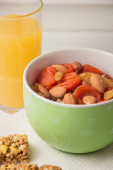 Granola cereal flakes with dried fruit, nuts in green bowl on white wooden table.