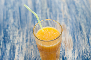Orange juice glass with straw on a blue wooden background of sea-green, top view close-up