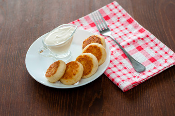 Cheese pancakes with sour cream on a white plate with a pink napkin and fork. Can be used for menu design.