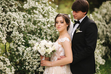 Handsome groom hug his bride in their wedding day. Background of flowering trees