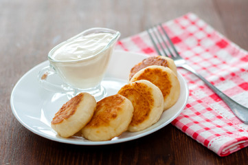 Cheese pancakes with sour cream on a white plate with a pink napkin and fork. Can be used for menu design.